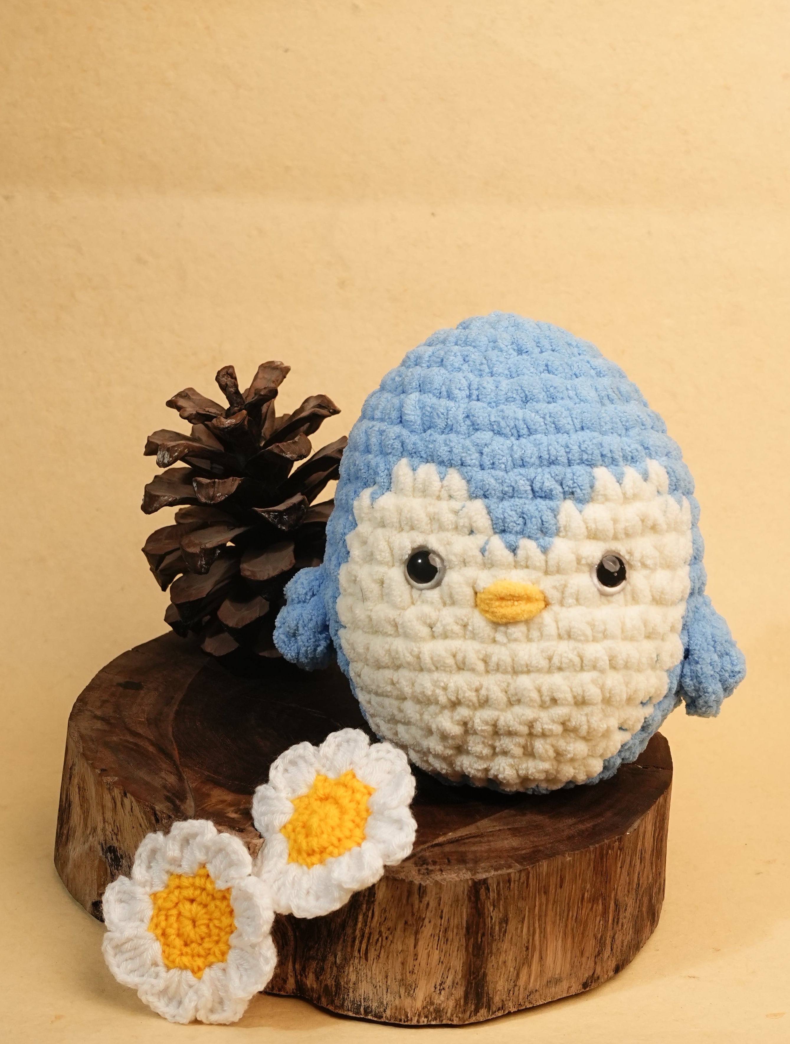 Crocheted bird figure with flowers and pinecones on a beige background